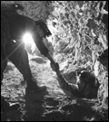 Black and white photo. One caver helping another come out of a squeeze.