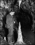 1920's picture with man in suit looking at a stalagmite.